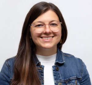 Headshot of female with long brown hair and glasses smiling and wearing jean jacket
