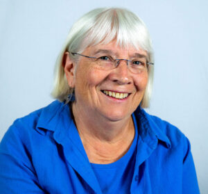 Woman with shoulder length white hair and glasses smiling