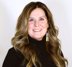 Headshot of woman with long brown hair smiling with a black turtleneck