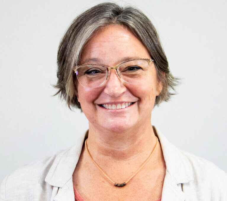 Headshot of a smiling woman, with short hair and glasses.